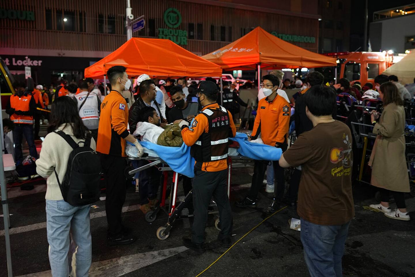 韩国梨泰院人踩人：图为2022年10月29日惨剧发生后，30日凌晨大批救援人员和消防员在意外现场救人。 从照片可见，一名看来意识仍然清醒的伤者，被抬到在街上临时搭建起来的帐篷。 （AP）