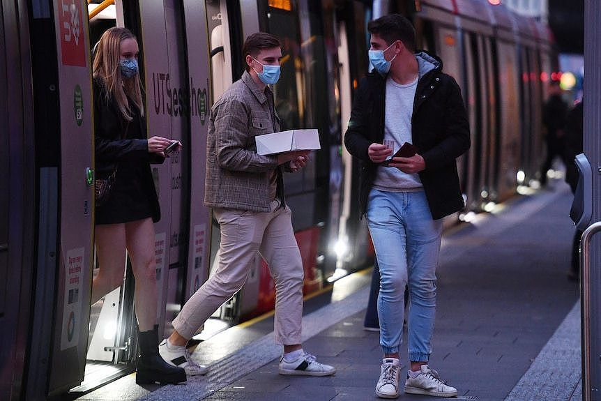 a group of young people hopping off a tram wearing face masks
