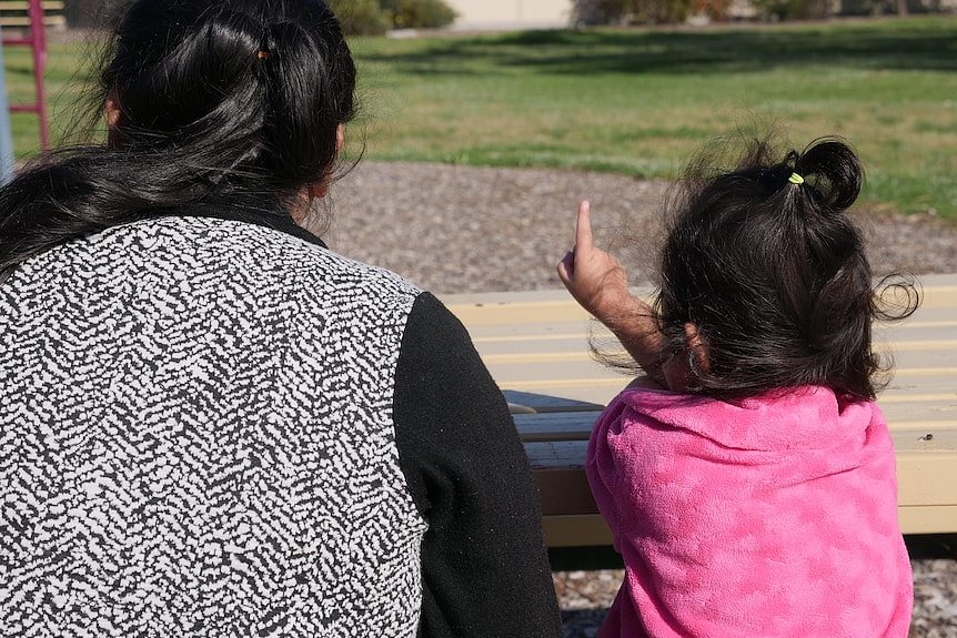 A woman and child in a park photographed from behind. 