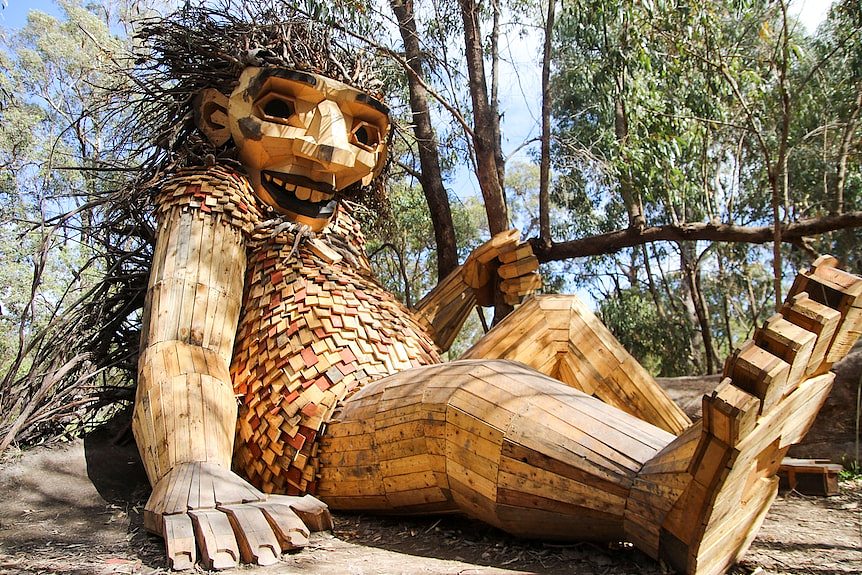 A massive human like wooden sculpture sitting amongst trees