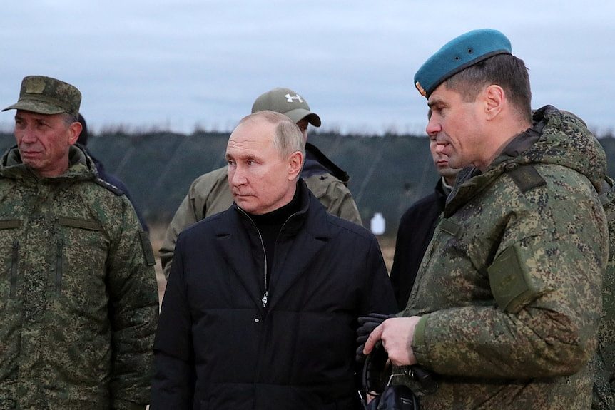 Putin stands with three men in army fatigues