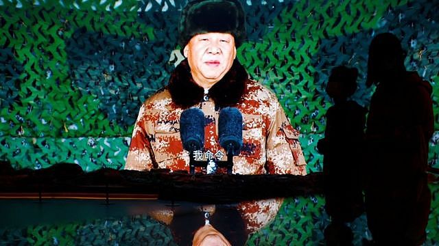 Visitors walk past a giant screen displaying Chinese President Xi Jinping delivering a speech to members of the Chinese People