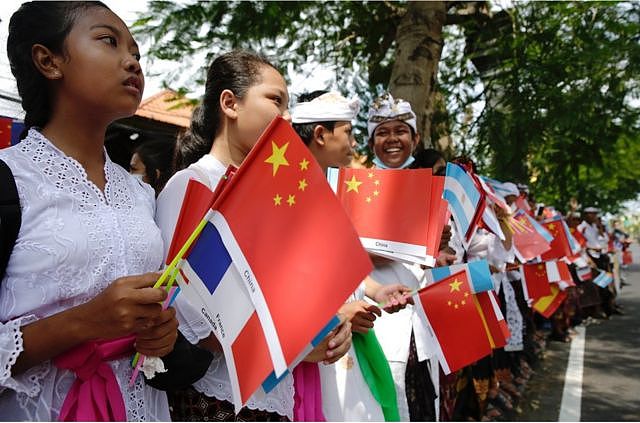 巴厘岛学生在国际机场附近的一条街道上，挥舞着G20成员国的旗帜，欢迎出席峰会的领导人抵达巴厘岛。