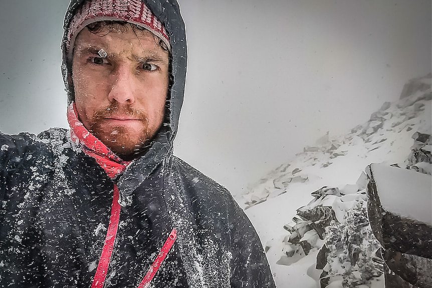 Man in a spray jacket on a mountain covered in snow.