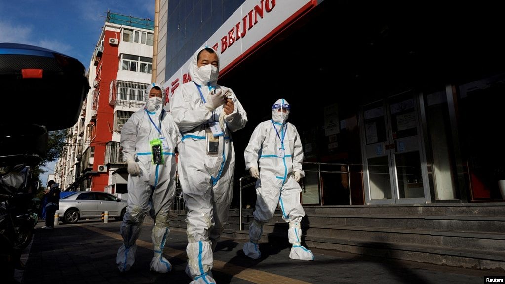 身穿防护服的人员行走在北京一个被封控的居民小区旁的街道上。（2022年11月12日）