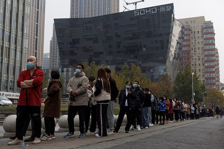 Picture of a long line of people wearing face masks on a street 