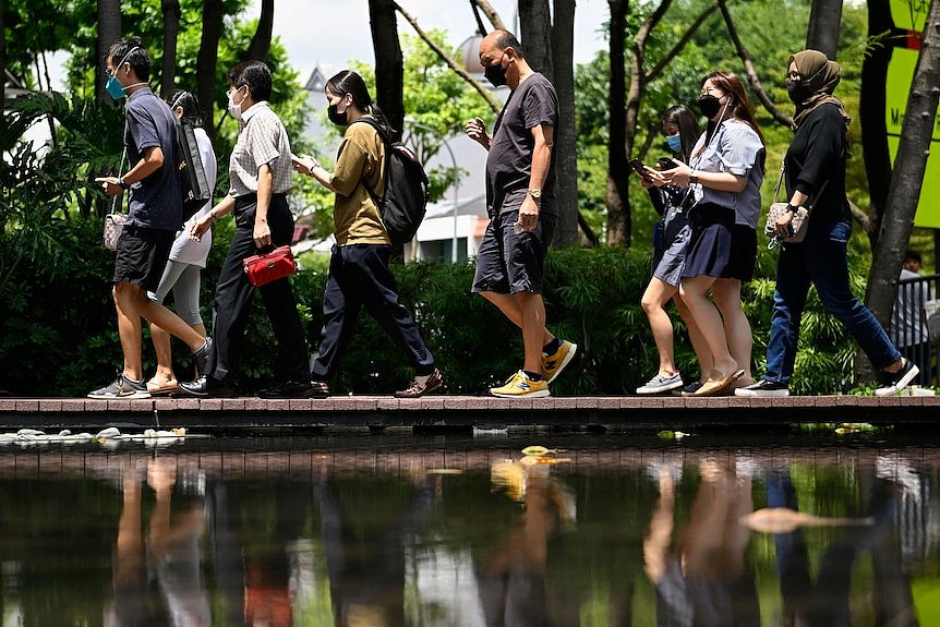 People walk on a bridge reflected in water wearing masks. 