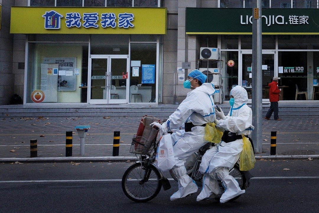 在中国北京，身穿防护服的防疫人员在街道上骑著电动脚车。（图取自路透社）