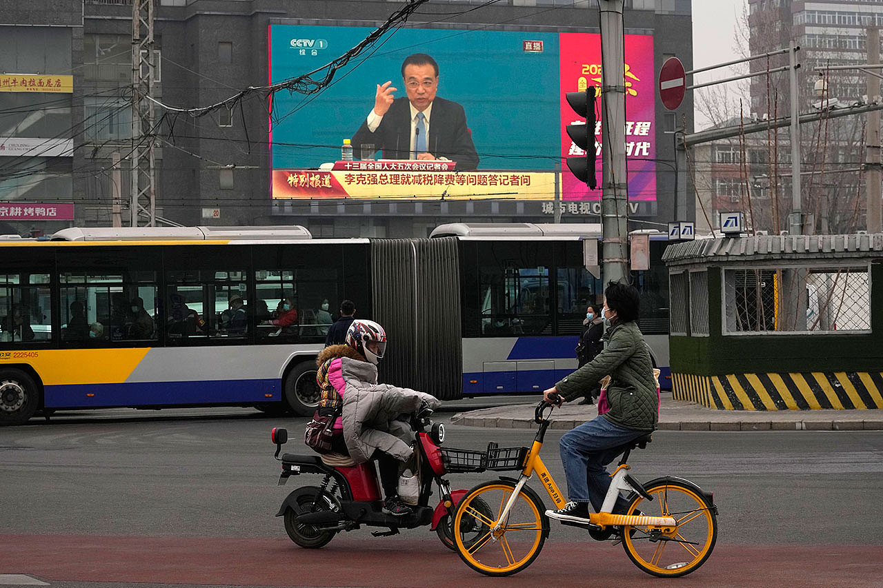 资料图片：北京，人们骑车经过十字路口的大屏幕，显示中国总理李克强在新闻发布会上的讲话。（美联社）