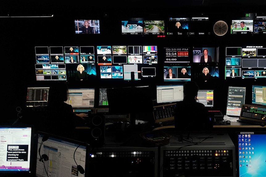 Wide shot inside studio control room with multiple TV monitors showing Leigh Sales and Laura Tingle on screen.