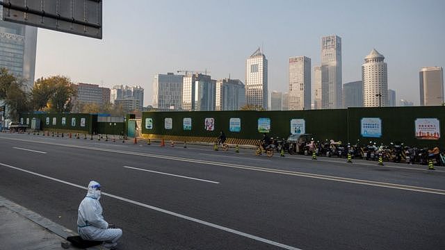 一名身穿防护服的北京防疫工作者坐在中央商务区 (CBD) 的人行道上