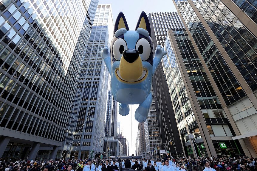 A giant inflatable Bluey floats between high-rises in the parade 