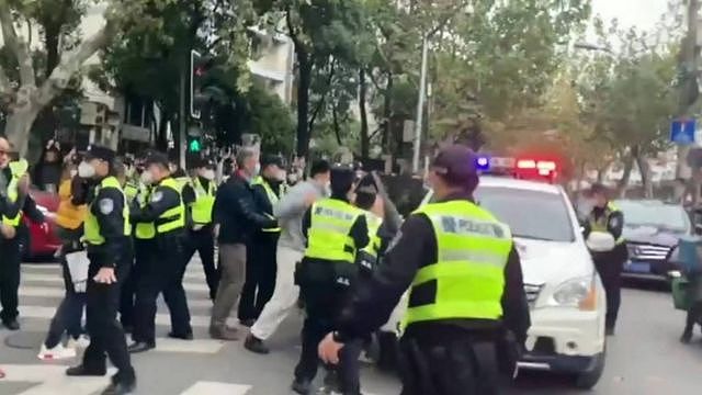 身穿荧光夹克的警察在上海一辆汽车旁与抗议者对峙