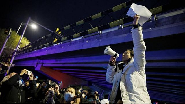 11月28日，在北京，在为乌鲁木齐火灾受害者守夜后，一名男子拿着白纸抗议当局的疫情封控措施。