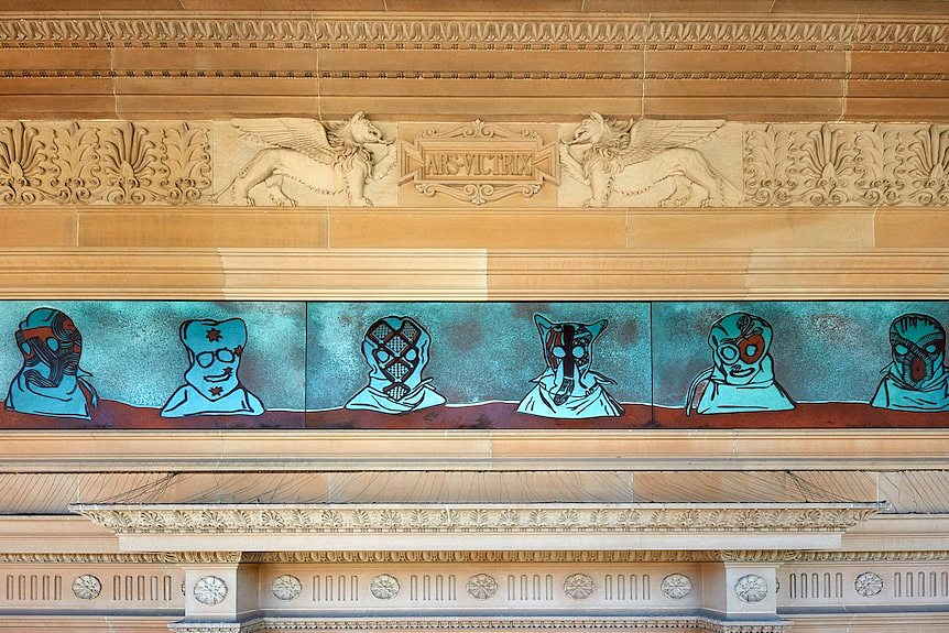 A panel made of metal depicting hooded figures, installed in above the entranceway to a classical-style building