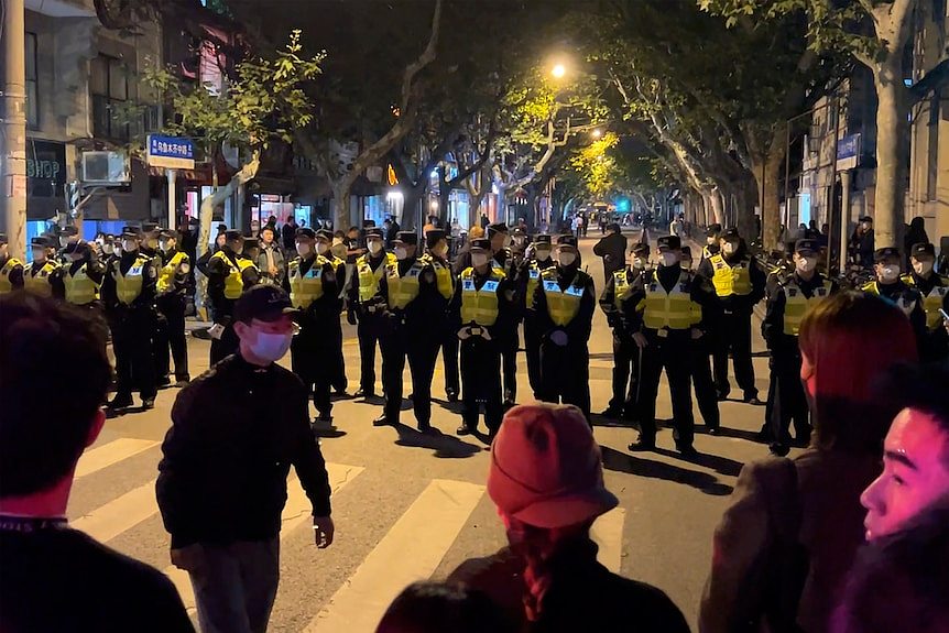 中国警察在街道上排成一排，阻挡聚集在人行横道另一边的抗议者。