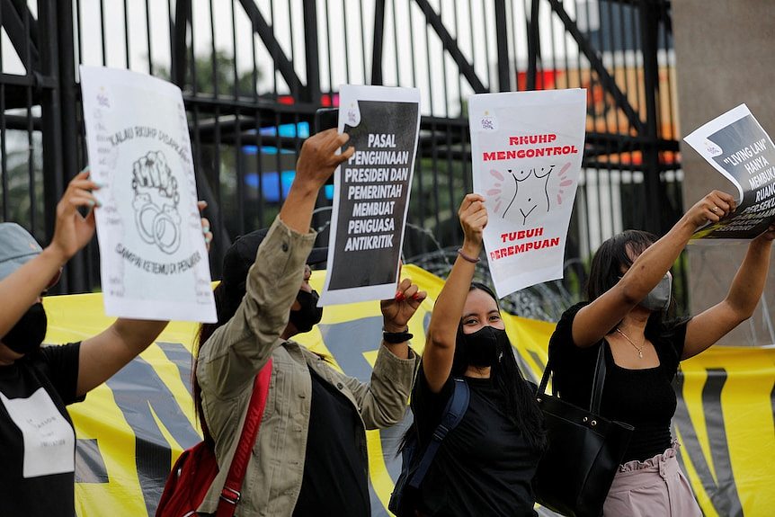 People hold up signs in Indonesian during a protest outside a gated building.