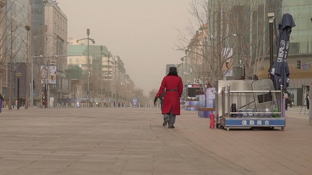 一名身穿红色外套的保安走过北京一条空无一人的购物街。