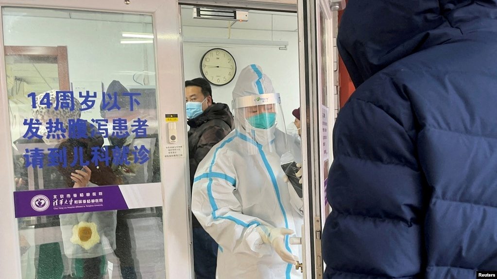 2022年12月15日，一名男子在北京一家医院的发热门诊门外排队等待。一位身着防护服的医务人员正准备关门。中国有关当局毫无预兆地宣布解封后，新冠肺炎的感染人数和死亡人数不断增加，引起人们的恐慌。