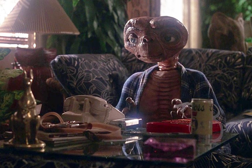 ET sits at a coffee table watching TV. 
