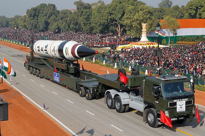 A missile the size of several cars is towed on the back of a truck down a street lined with onlookers