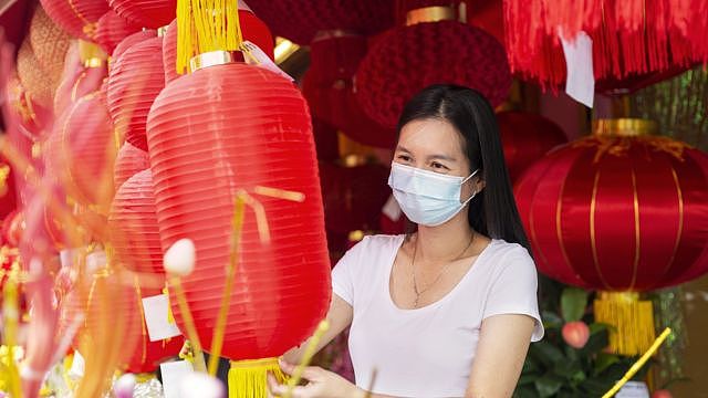 一名戴口罩女子在市场上挑选传统的红灯笼，为在农历新年期间装饰自己的家做准备