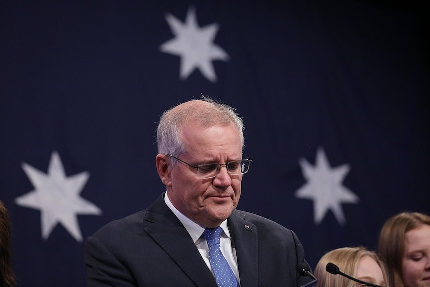 Outgoing prime minister Scott Morrison looks glum standing in front of an Australian flag after the 2022 federal election.