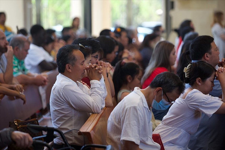 people pray as the stand in the pews of St Mary's Cathedral in Perth