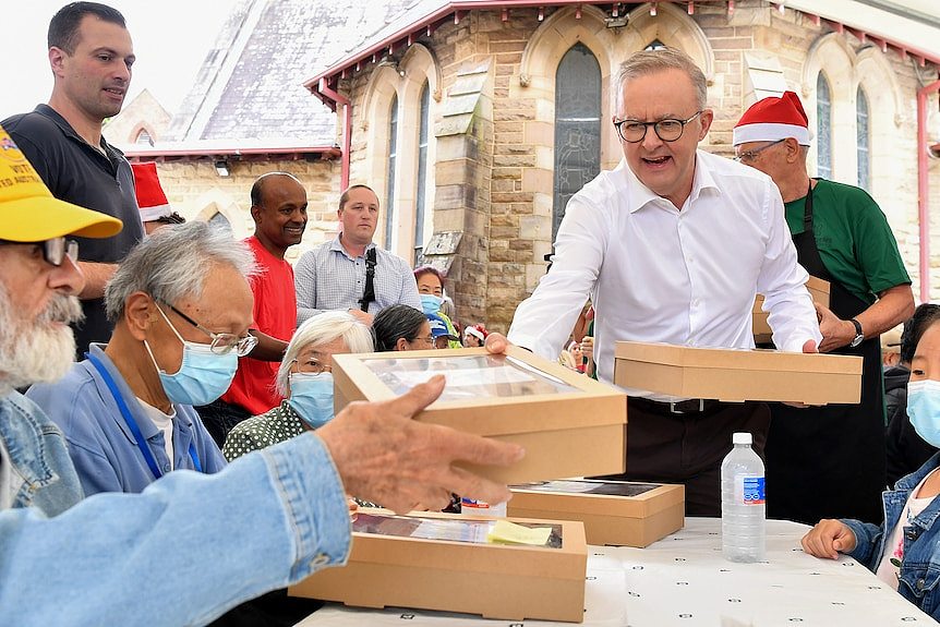 Anthony Albanese in a white shirt hands out lunch to people at a table at Rev Bill Crews in Sydney