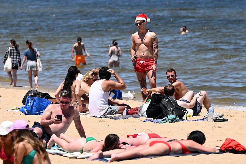 people in swimwear stand on St Kilda Beach and wade in the water