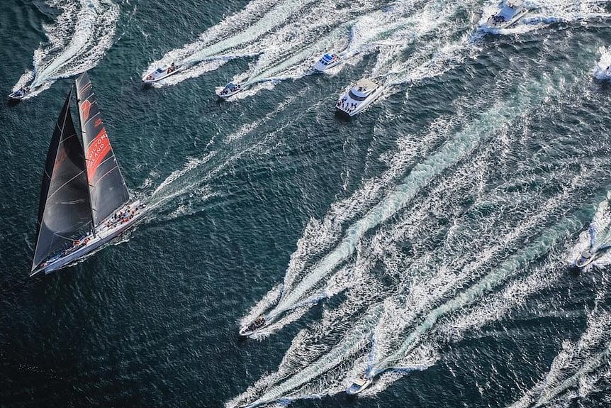 Large sailboat with other watercraft in pursuit as seen from overhead.