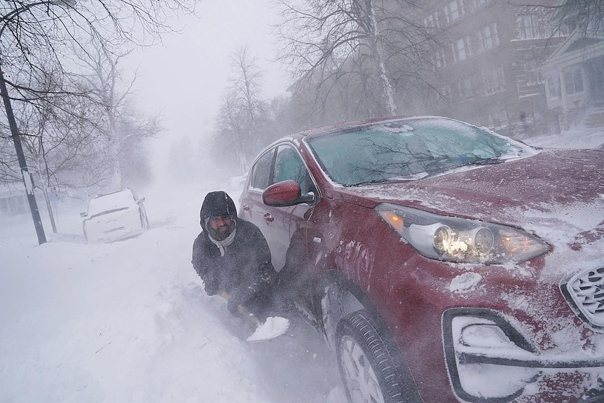 A man digs in deep snow surrounding a red car