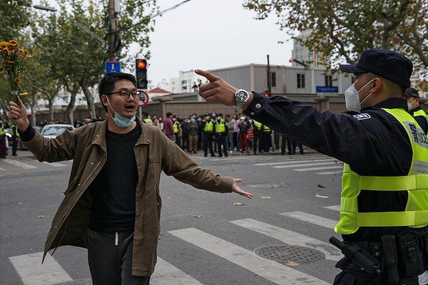 一名举着花的男子在街头发表演讲，一名警察正在要求他离开