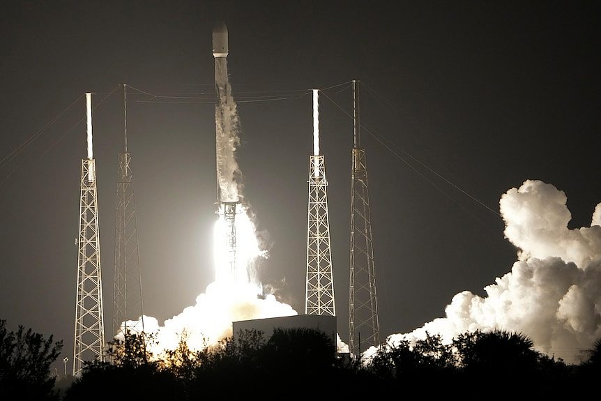 A rocket ship launches in a cloud of smoke at night. 