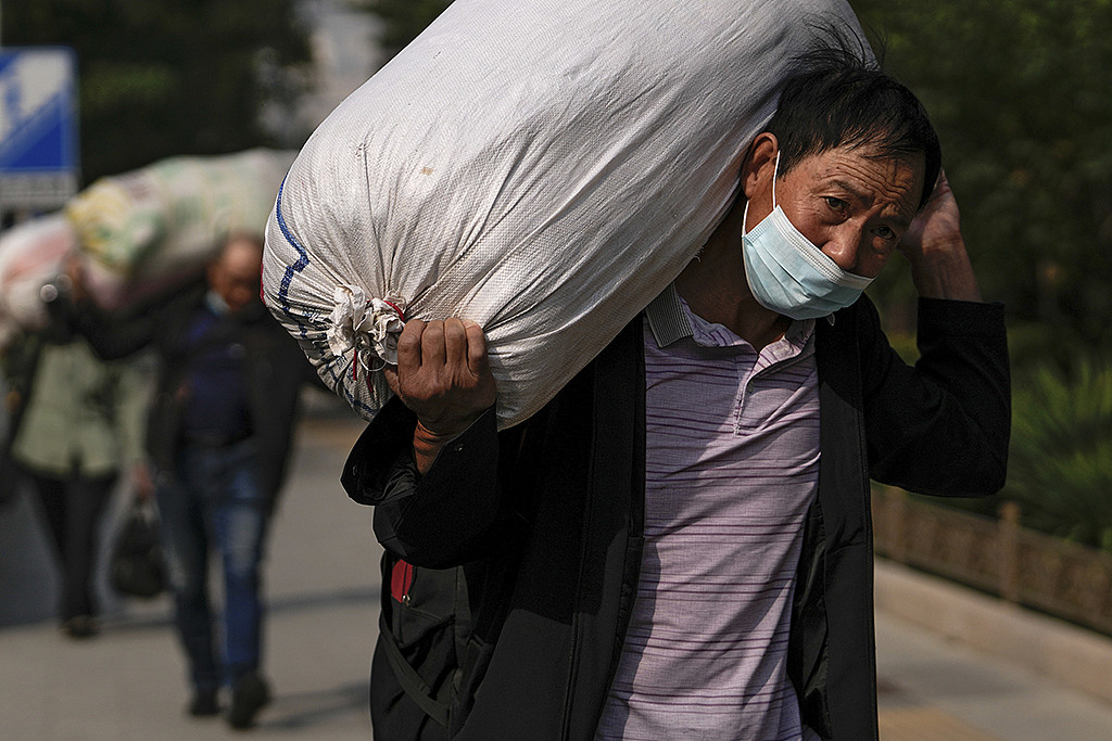 农民工背负重袋，走在北京街头。摄于2022年9月27日。(美联社)