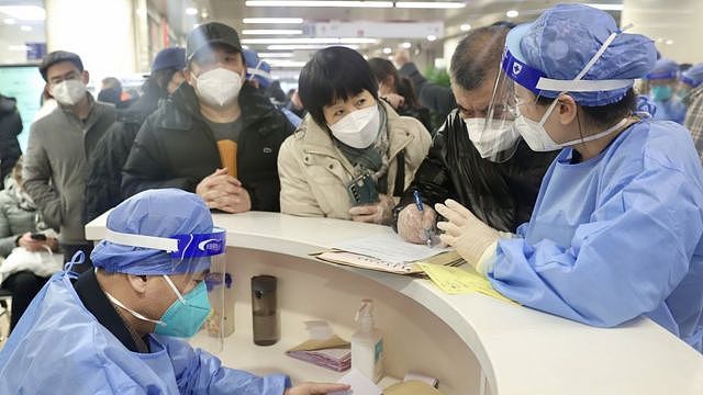 北京朝阳医院本部急诊大厅候诊区患者与家属围着医护人员查询情况（中新社图片27/12/2022）