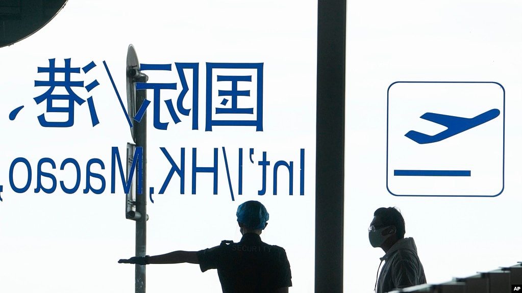 资料照 - 2022年8月24日，北京机场一名机场安保指示一位戴口罩的旅客继续前往安检口进行安检。