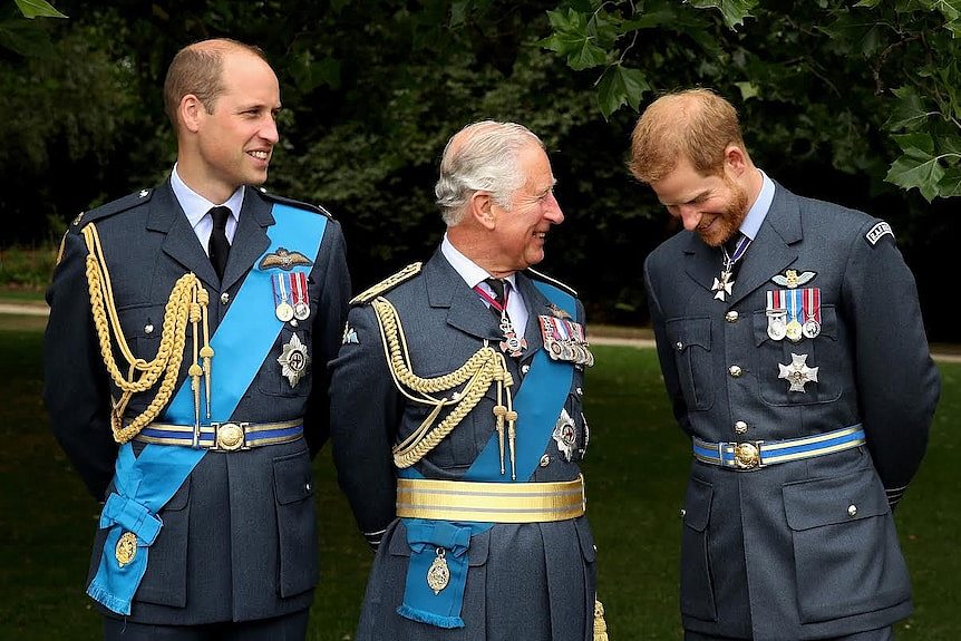 Prince Charles grinning while standing between his sons William and Harry