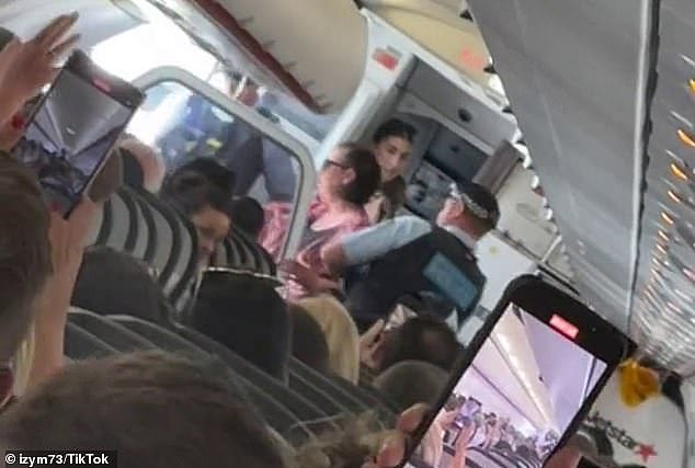 A passenger who uploaded the footage to TikTok told viewers the three-hour flight had been delayed for an hour over the ordeal (pictured, the woman is removed by police officers)