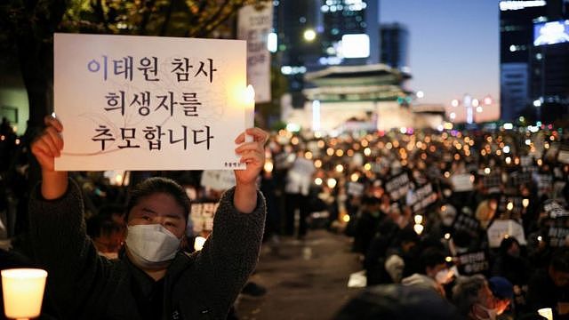 首尔广场一场悼念梨太院踩踏事件的烛光晚会上一位女士举起悼念标语（5/11/2022）