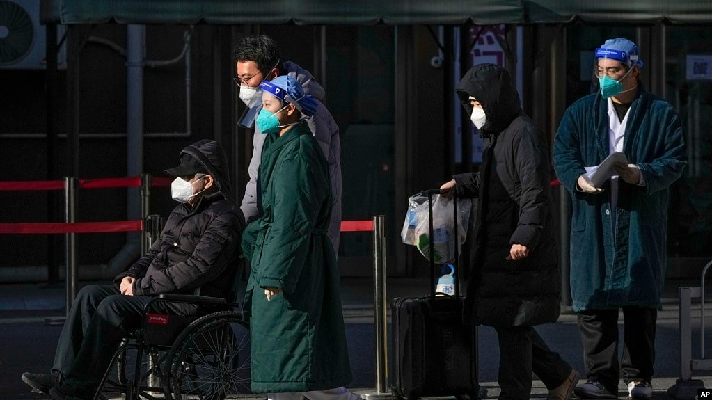 资料照 - 2022年12月19日，北京一所医院的医护人员身着防护服护送一位坐轮椅的老年病人离开发热门诊部。中国卫生官员表示，中国的官方统计只把那些直接死于肺炎或呼吸衰竭新冠病毒感染者列入新冠致死名单。