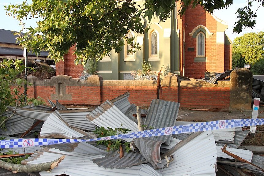 Police tape across a pile of corrugated iron in front of a damaged brick church.