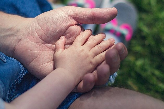 Adult male hand holds hand of a child.