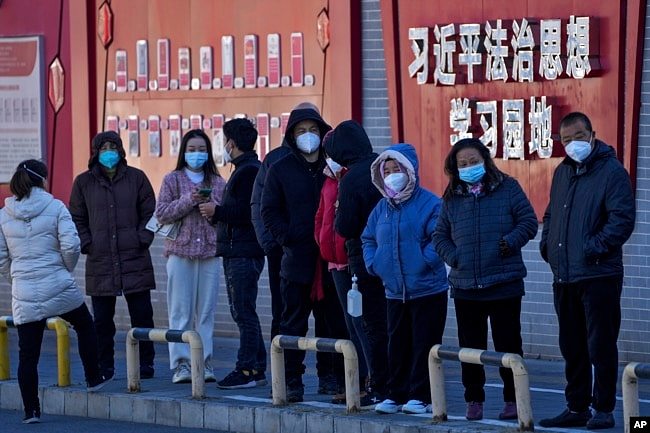 北京市民在宣传习近平思想的标语墙前排队等候接受核酸检测。（2022年12月5日）