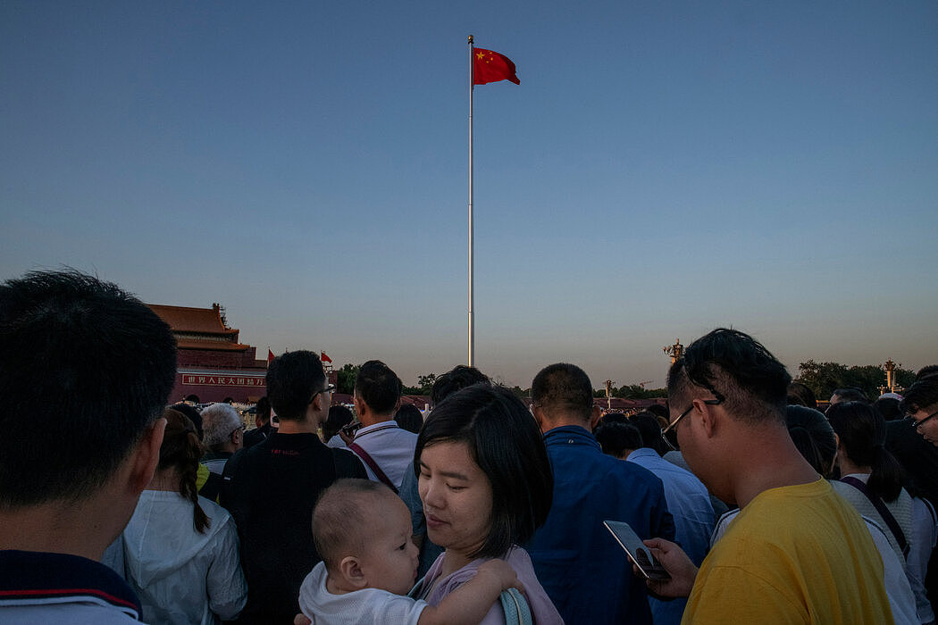 一名女子抱着孩子观看北京的升旗仪式，摄于2018年。越来越多的中国女性为实现自己的抱负放弃生孩子。