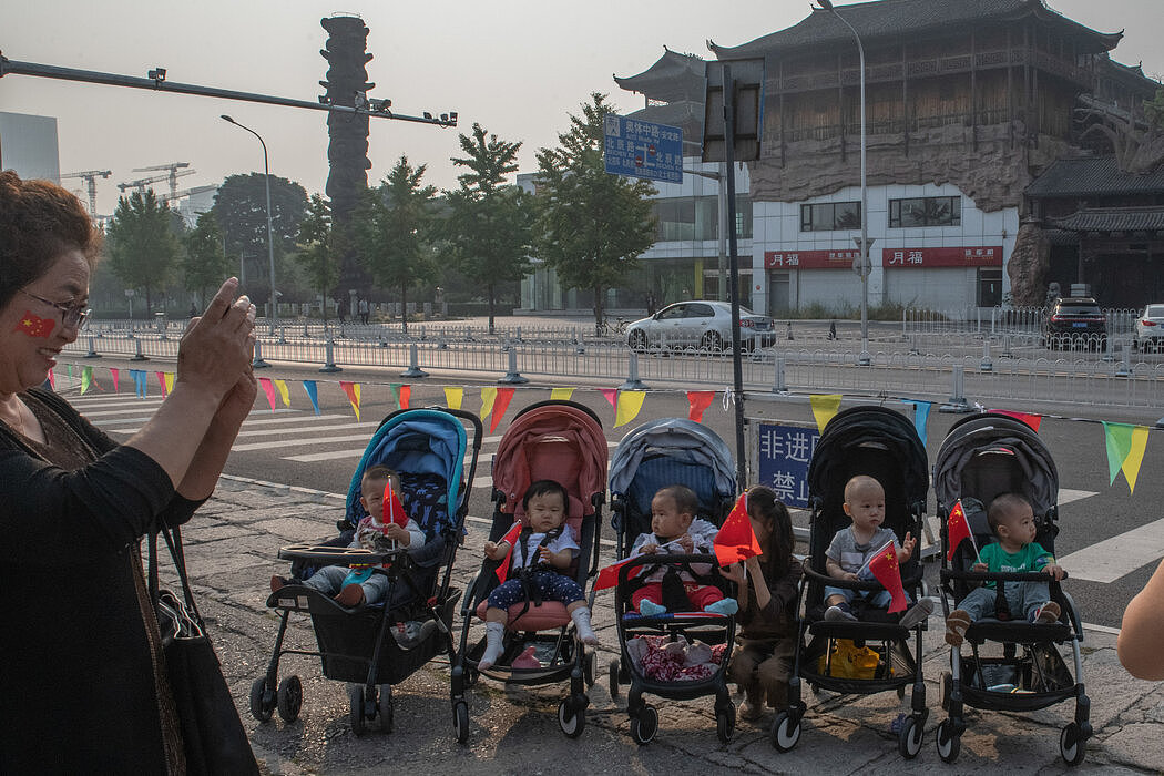 坐在婴儿车上手持国旗的儿童，摄于北京2019年国庆节期间。出生率下降和人口老龄化已使中国陷入人口困境。