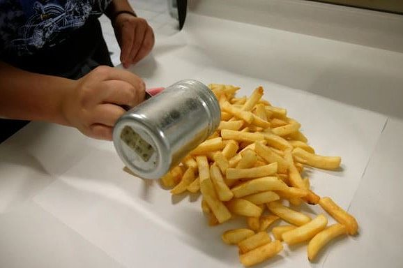 Person shakes salt onto hot chips sitting on wrapping paper
