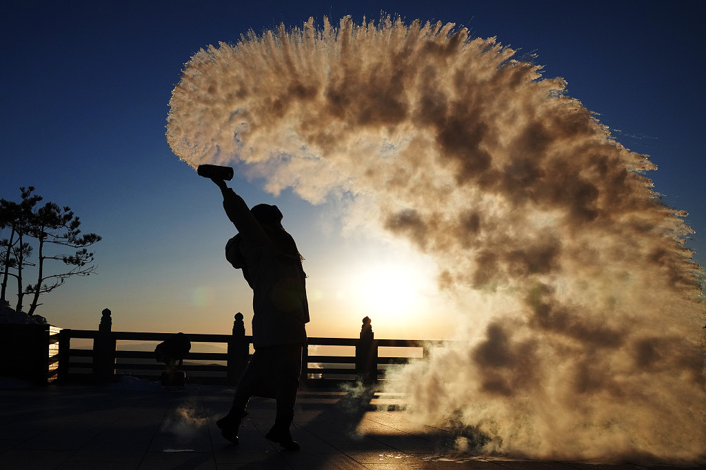 在抚远市东极阁，游客在日出时玩「泼水成烟」。 新华社