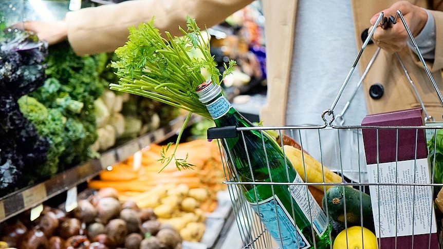 A person shopping at Australian grocery store, with a basket full of sparkling water, fruits and vegetables.