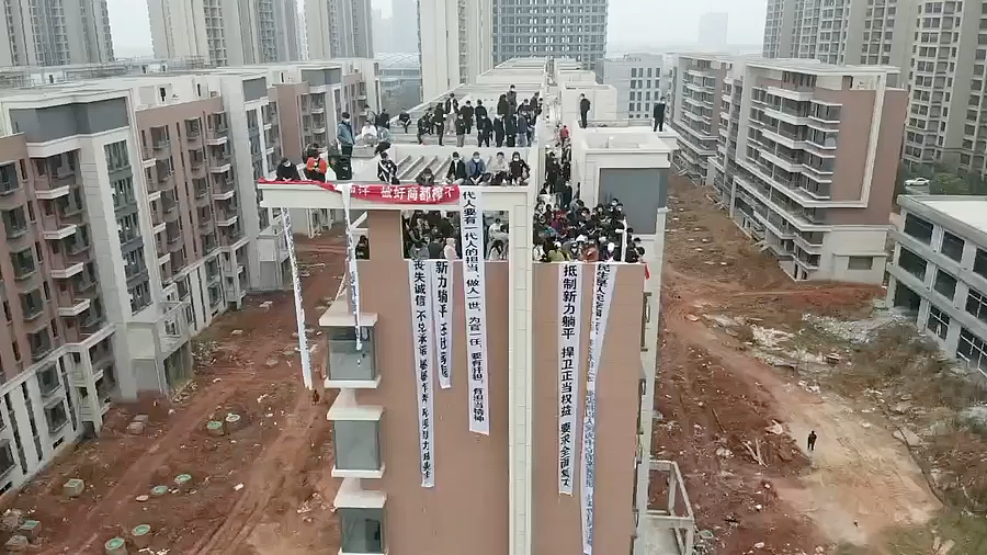 在一栋未完工的公寓楼顶上，购房者要求全面恢复施工。最左边的条幅上写着：“丧失诚信 不兑承诺 屡屡作秀 无视新力城业主”。